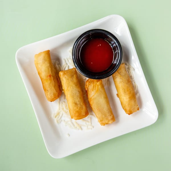 Four golden-brown spring rolls with a side of red dipping sauce on a white rectangular plate.