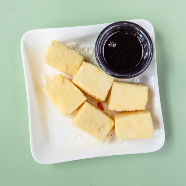 Six rectangular pieces of fried tofu with a small bowl of dark dipping sauce on a white plate.