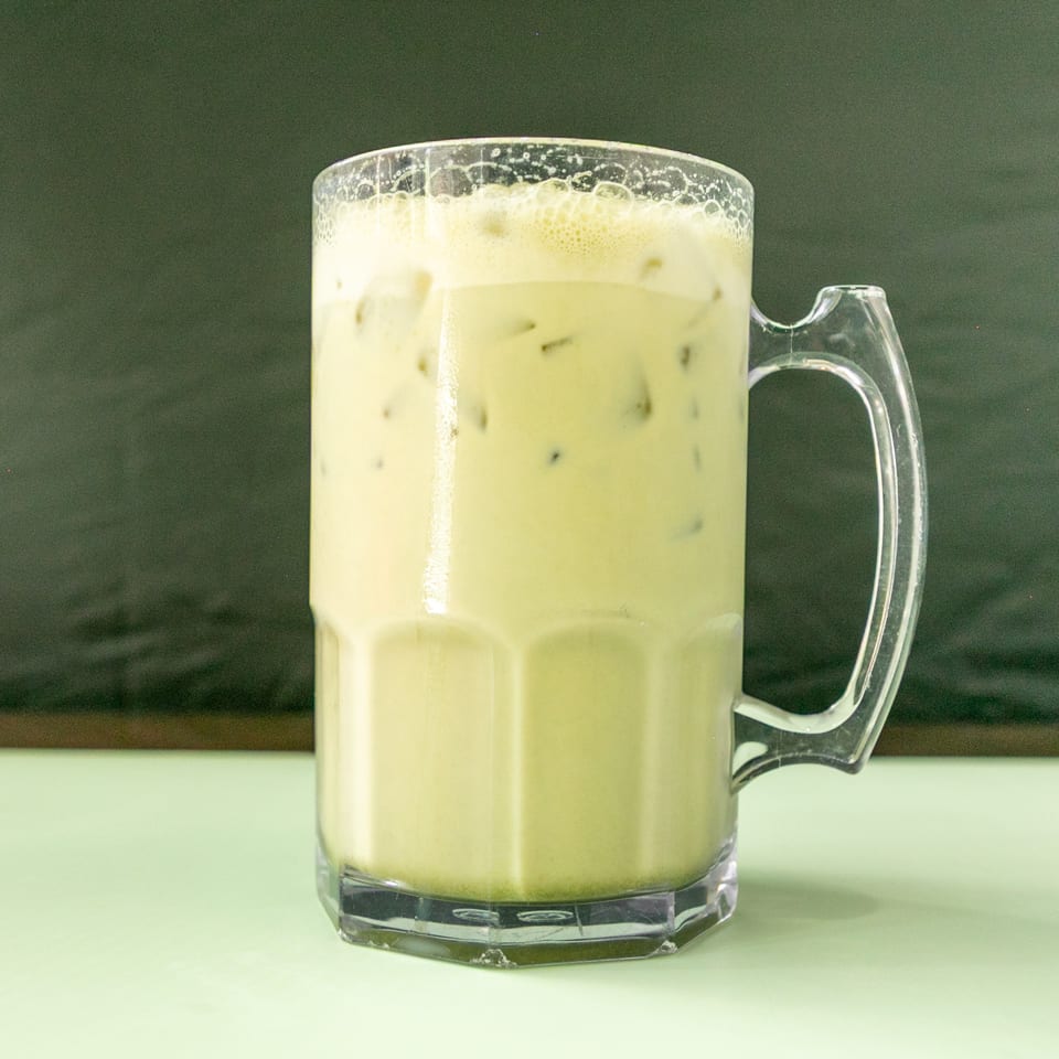 Iced matcha latte in a clear mug with a handle, on a light green table.
