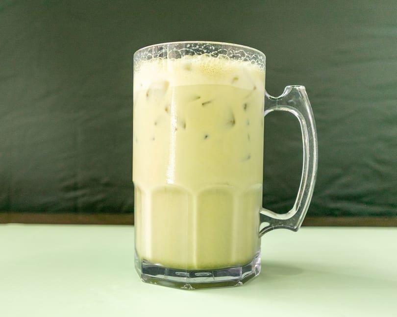 Iced matcha latte in a clear mug with a handle, on a light green table.