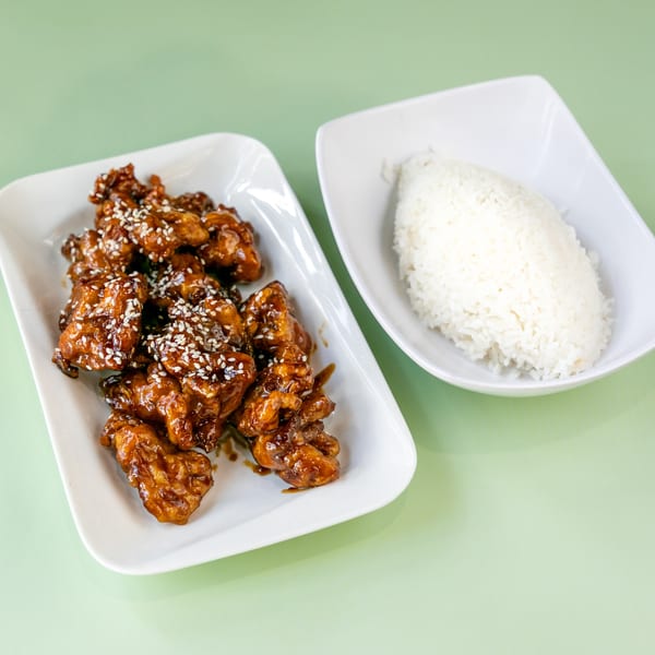 Sweet and sour chicken with sesame seeds and a side of white rice on a light green background.