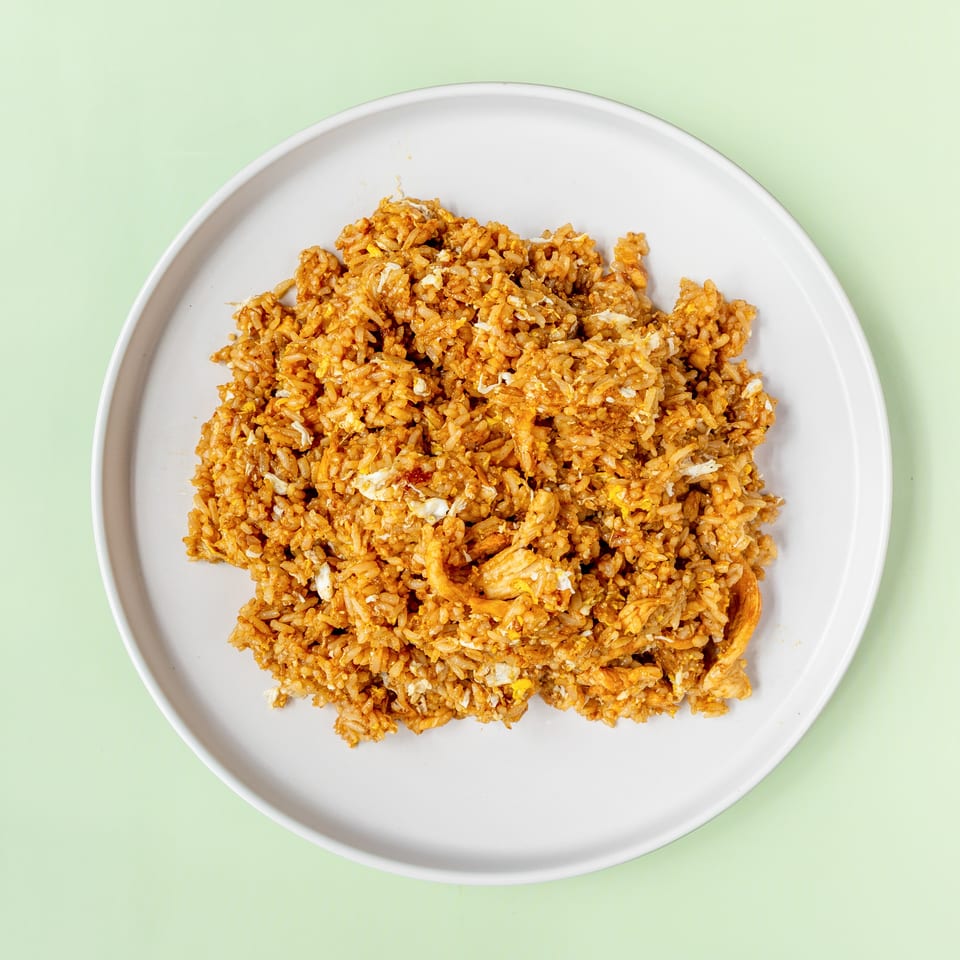 A white plate filled with golden-brown fried rice, featuring visible pieces of egg and chicken.