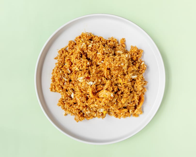 A white plate filled with golden-brown fried rice, featuring visible pieces of egg and chicken.