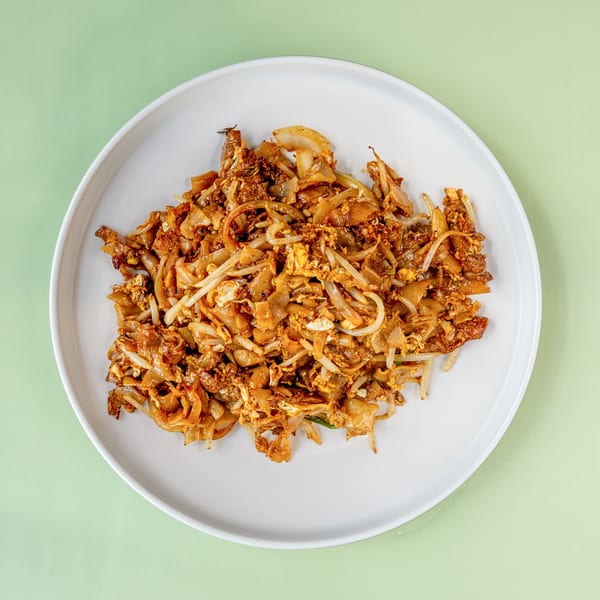 A white plate filled with Char Kway Teow, a stir-fried noodle dish with bean sprouts and egg.