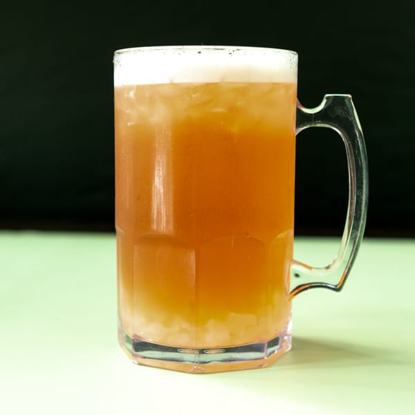 A large mug of iced tea with a foamy top sits on a light green surface.