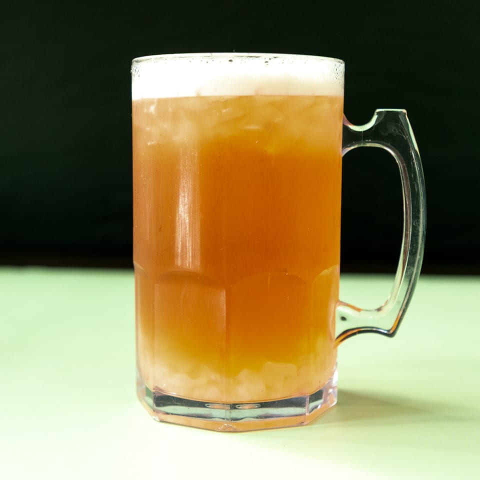 A clear mug filled with an amber-colored drink, ice, and a foamy head.