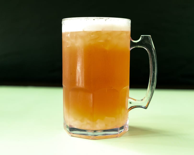 A clear mug filled with an amber-colored drink, ice, and a foamy head.