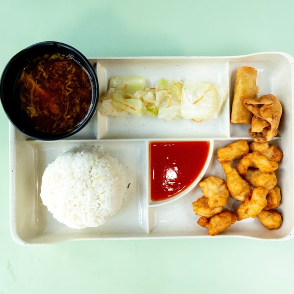 A divided tray with hot and sour soup, rice, sweet and sour chicken, egg roll, wonton, and cabbage.