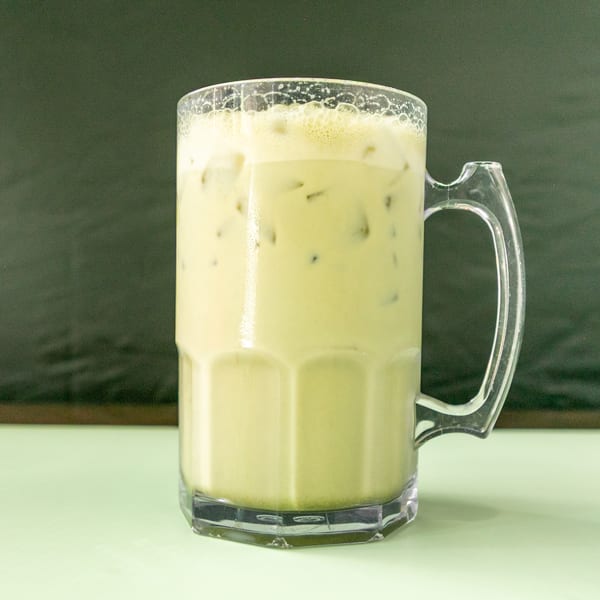 Iced matcha latte in a clear mug with a handle, on a light green table.