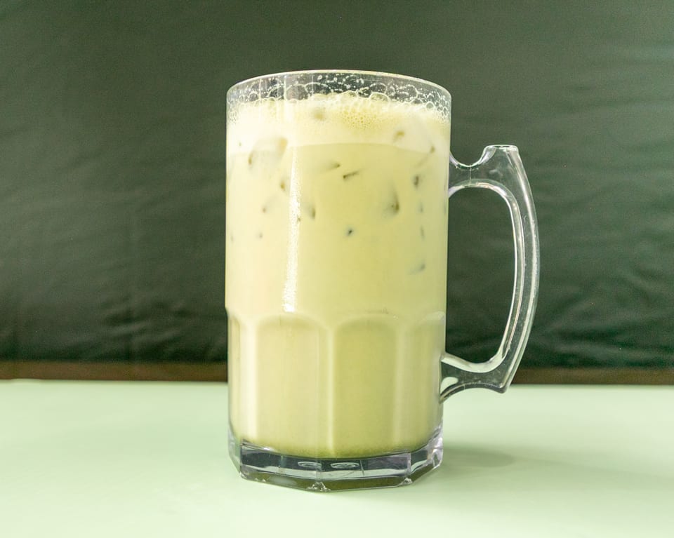 Iced matcha latte in a clear mug with a handle, on a light green table.