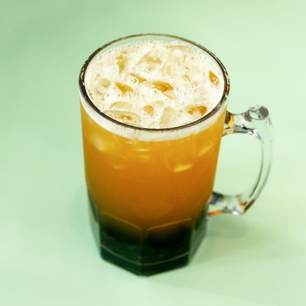 A large glass mug filled with an iced orange drink and a foamy top.