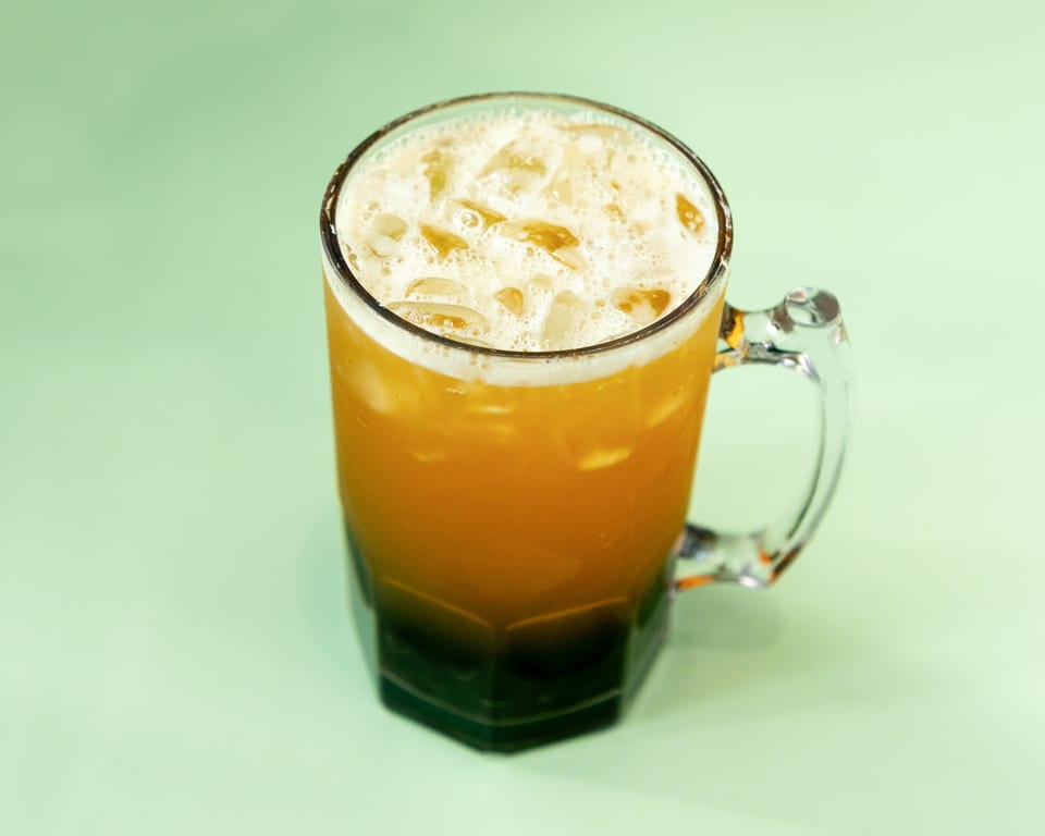 A large glass mug filled with an iced orange drink and a foamy top.