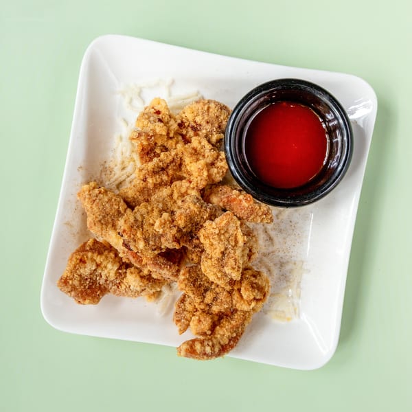 Crispy fried chicken pieces with a side of red dipping sauce on a white rectangular plate.