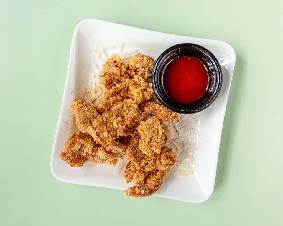 Crispy fried chicken pieces with a side of red dipping sauce on a white rectangular plate.