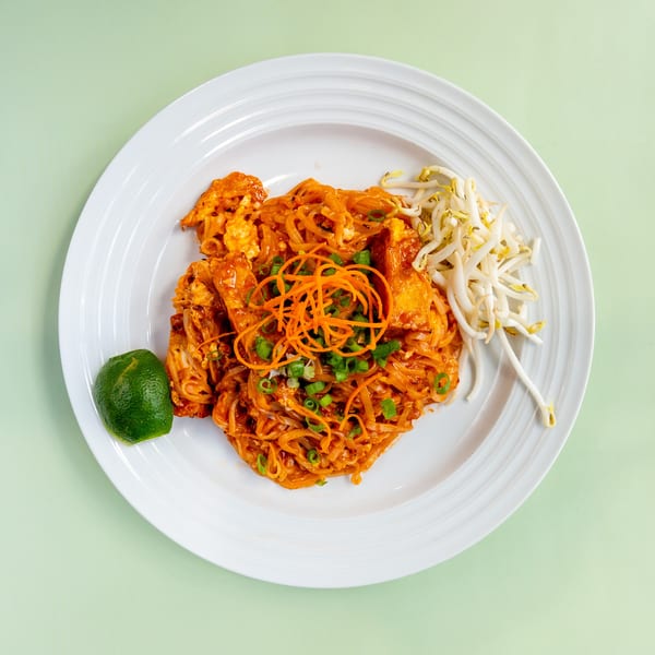 Pad Thai noodles with chicken, bean sprouts, shredded carrots, green onions, and a lime wedge.